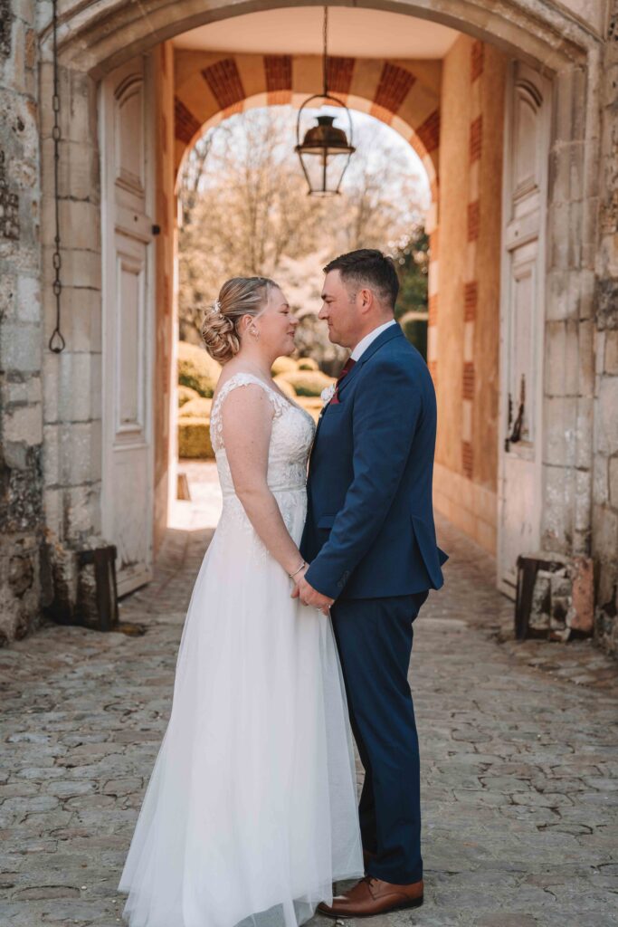 couple de marié se regarde en se tenant la main devant une entrée de chateau