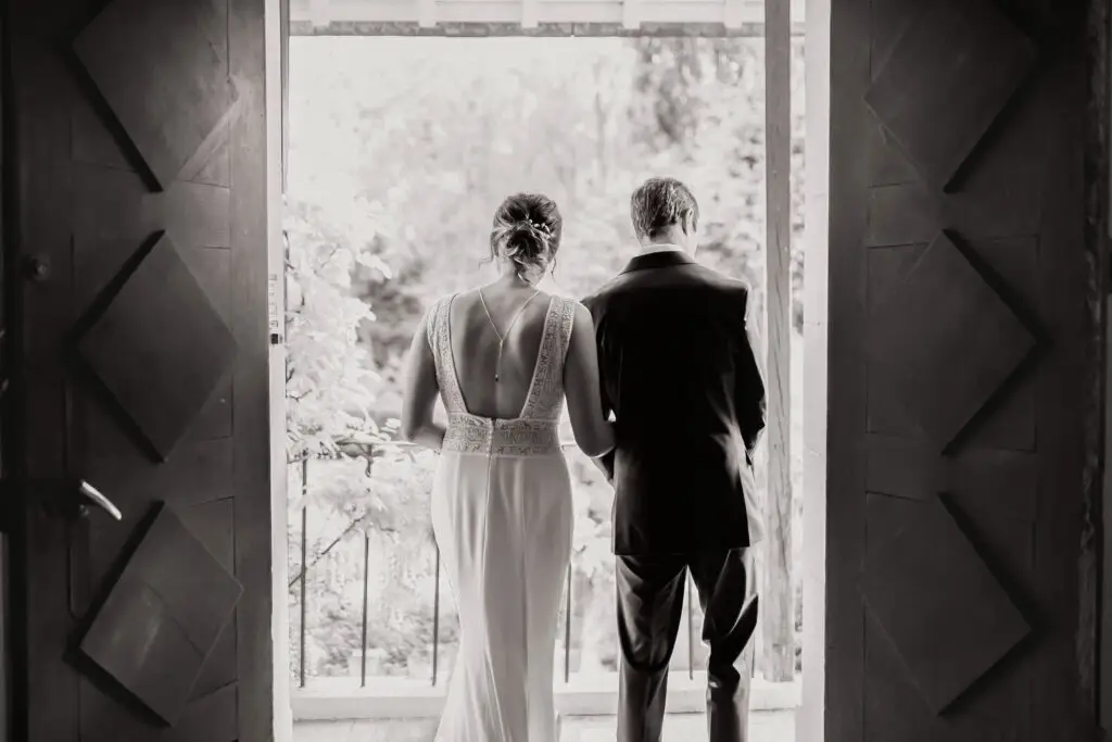 un couple de mariés de dos en noir et blanc dans le passage d'une porte de chateau photographe mariage Normandie