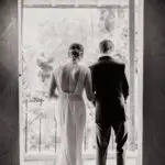 un couple de mariés de dos en noir et blanc dans le passage d'une porte de chateau photographe mariage Normandie