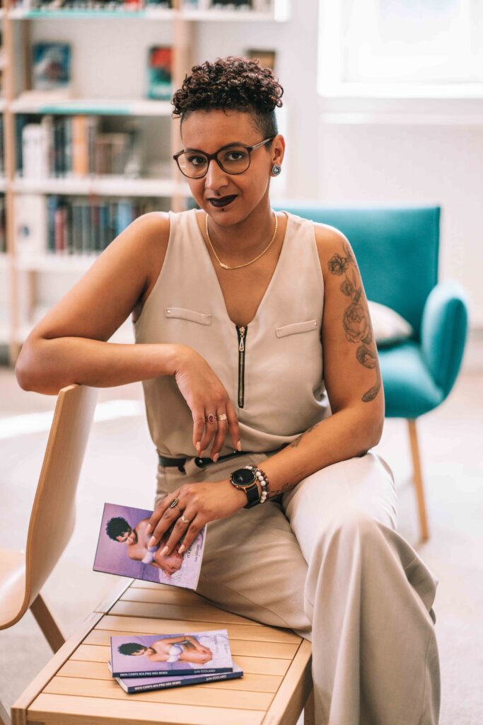 Femme assise sur une table dans une bibliothèque habillé en beige tien un livre dans ses mains et pose regard vers l'objectif Séance photo professionnel
