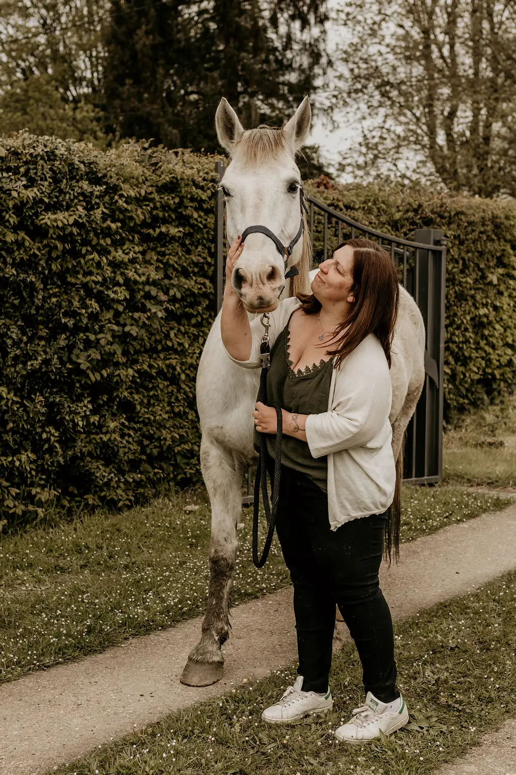 photographe en Normandie pose avec son cheval blanc dans une allée avec un portail en fond, photographe Normande